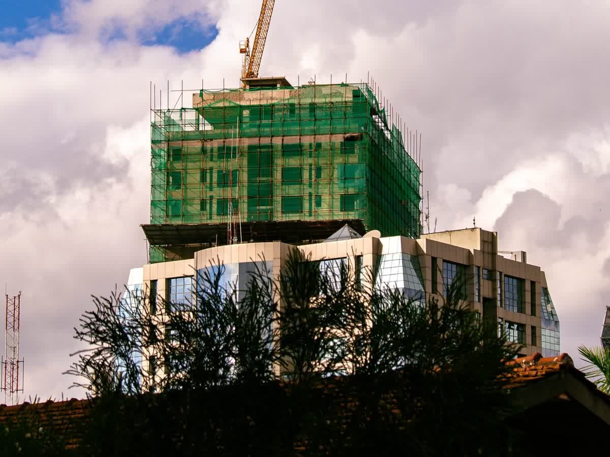 Commercial tower under construction with crane and safety netting above completed lower floors